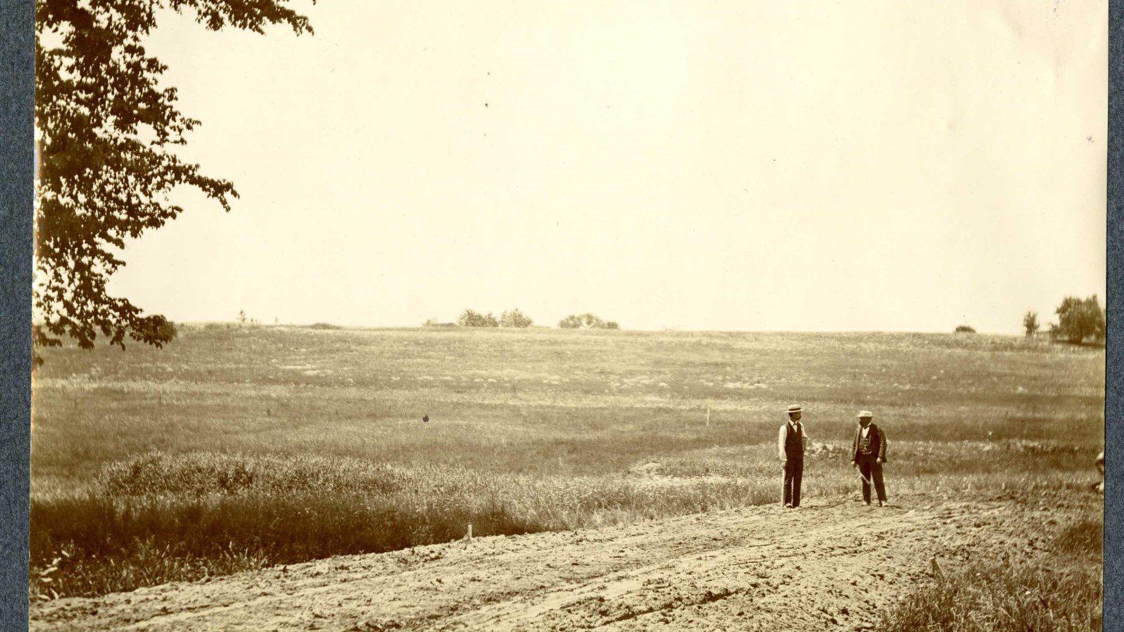 Black and white of dirt road at end of grassy hill with two people standing on it