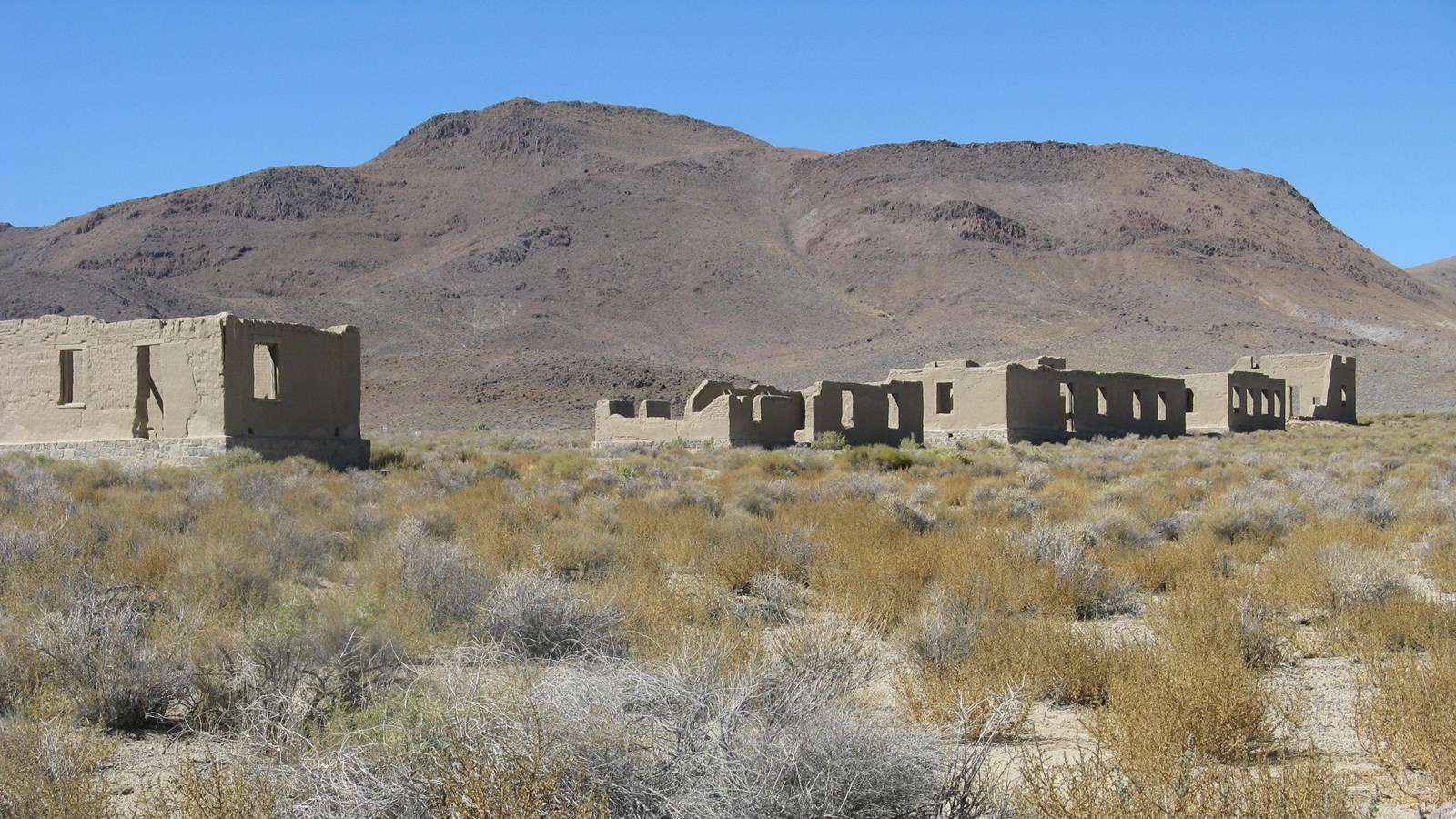 Partial walled ruins stand in a vast desert setting.