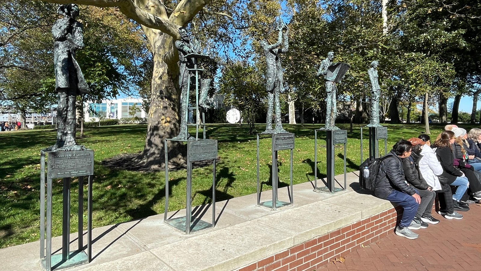 Five metal sculptures are displayed by a walkway on Liberty Island