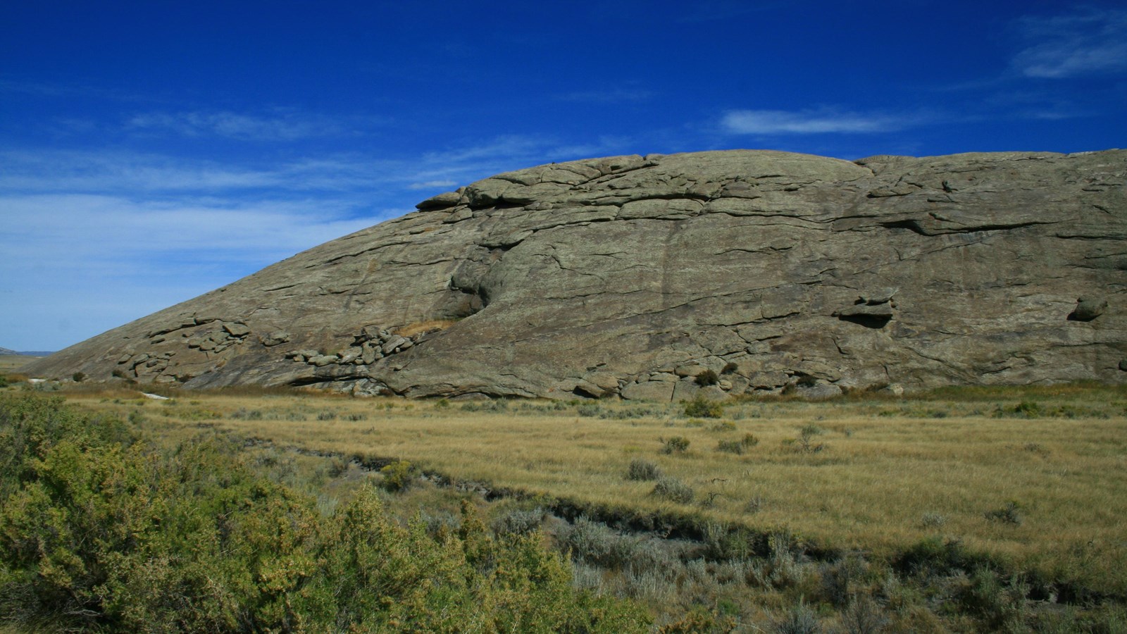A long smooth green-brown buttress set against a bright blue sky, and grassy valley.