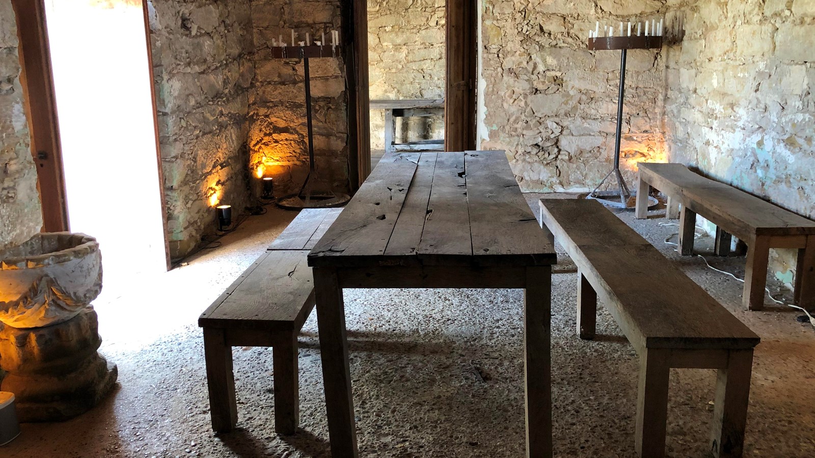 A wooden table sits in the middle of a small room with stone walls.