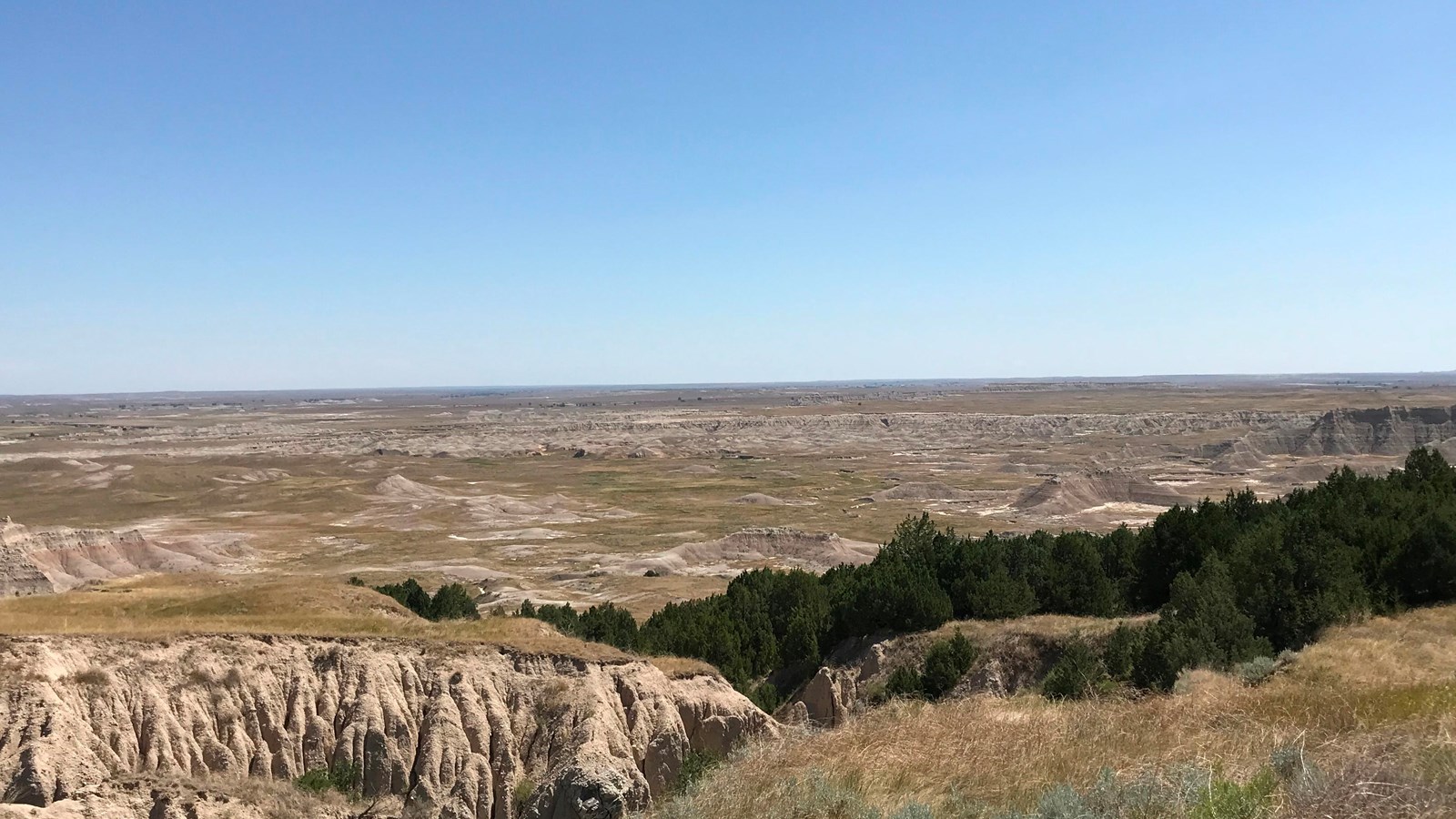 an expansive basin of mixed-grass prairie and badlands formations beneath blue sky.