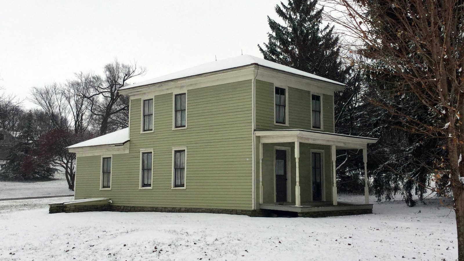 A green two story house has white trim and a porch.