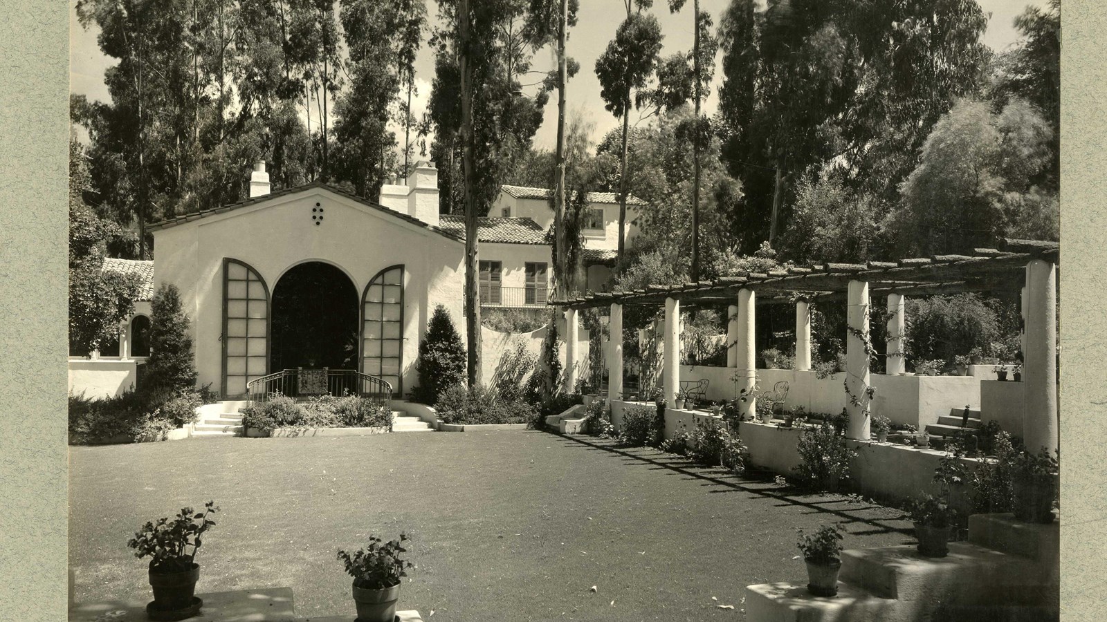 Black and white of flat garden in yard with white columns lined with potted plants