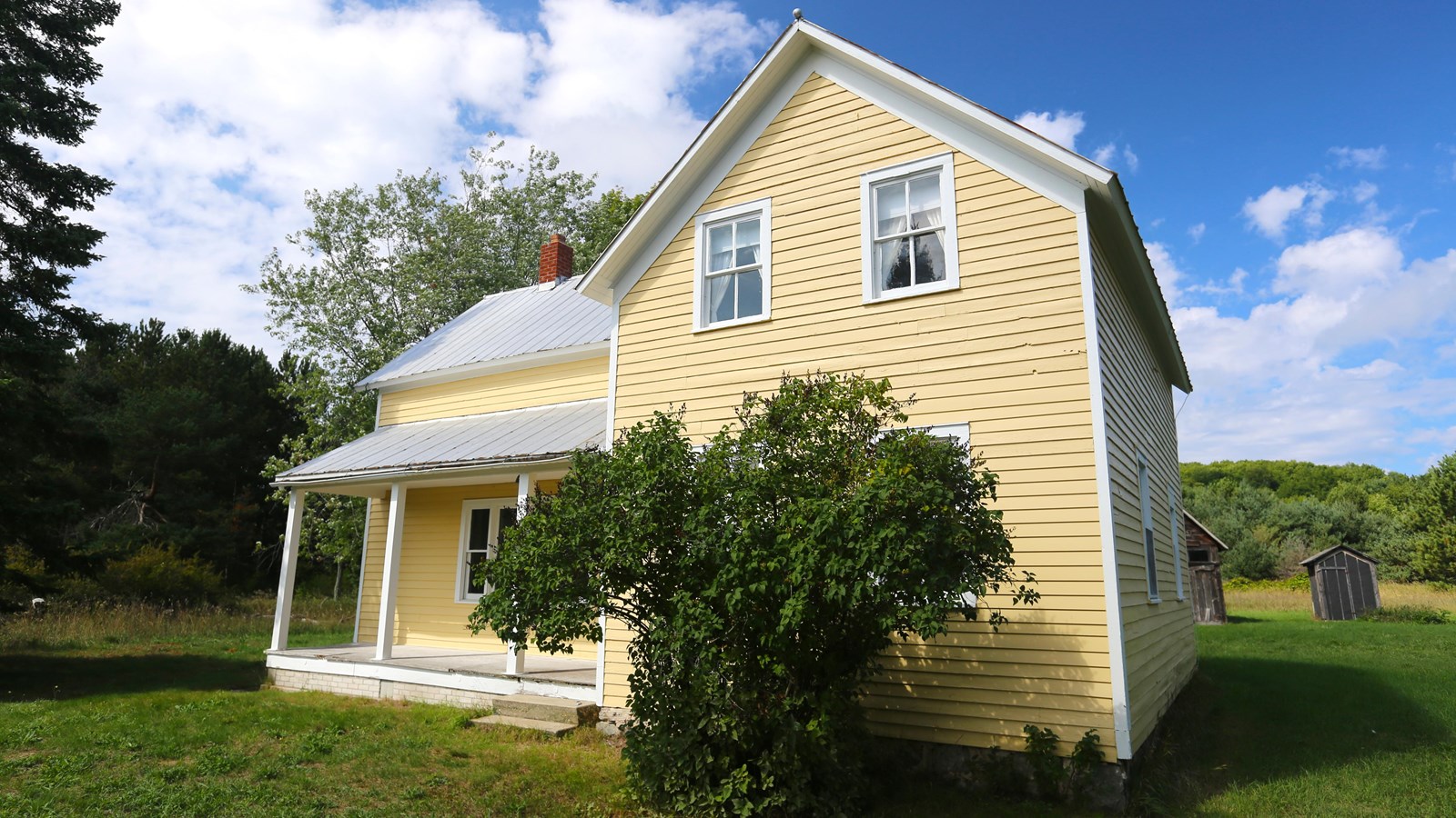 Yellow, clapboard, gabled farmhouse with a covered porch