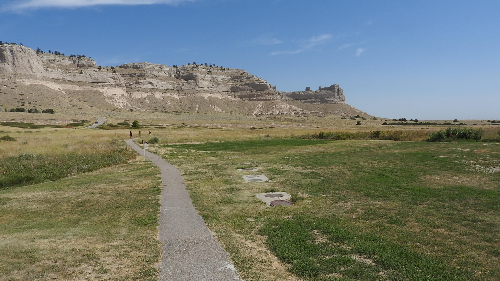 A paved trail leads through prairie grasses towards interesting rock formations.