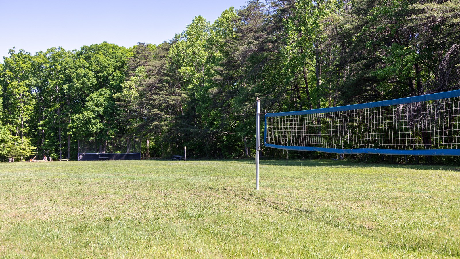 A volleyball net is set up in a grassy field. In the distance is a baseball diamond.