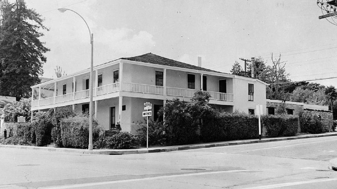 Black and white photo of the exterior corner of a two-story building surrounded by hedges.