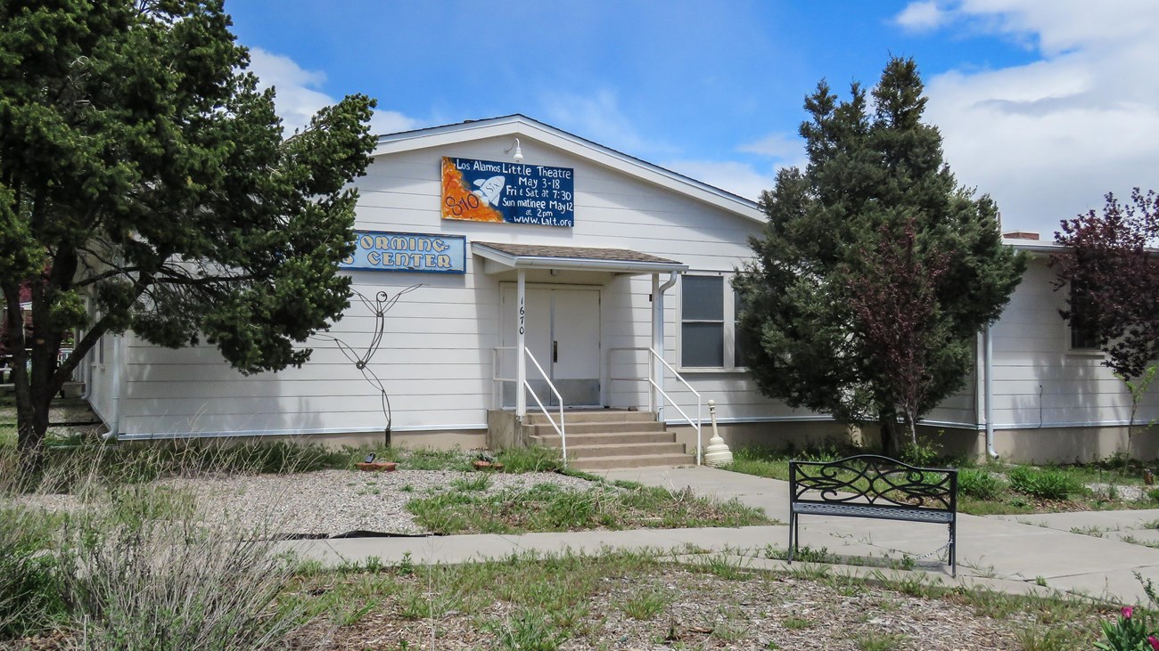 A wooden, white building with a blue and orange sign with white text.