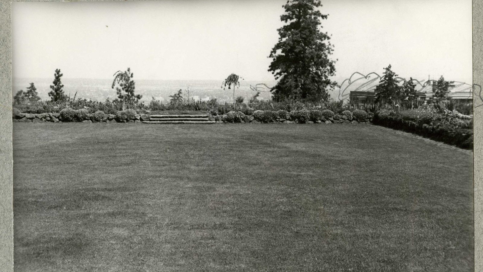 Black and white of flat grassy area with shrubs around edges