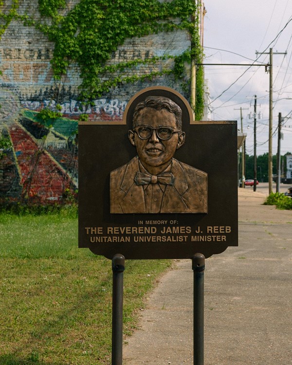 a metal sign with a etching of a smiling man in a suit and tie and wearing glasses.