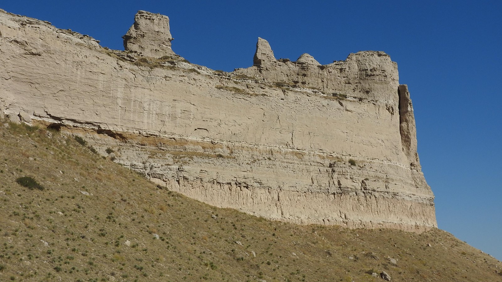 A large rock formation with visible strata and large chunks of rock at its base.