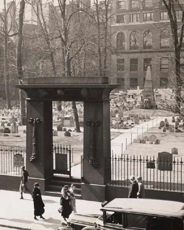 Historical photo of a burying ground with an granite gate and headstones in the background.