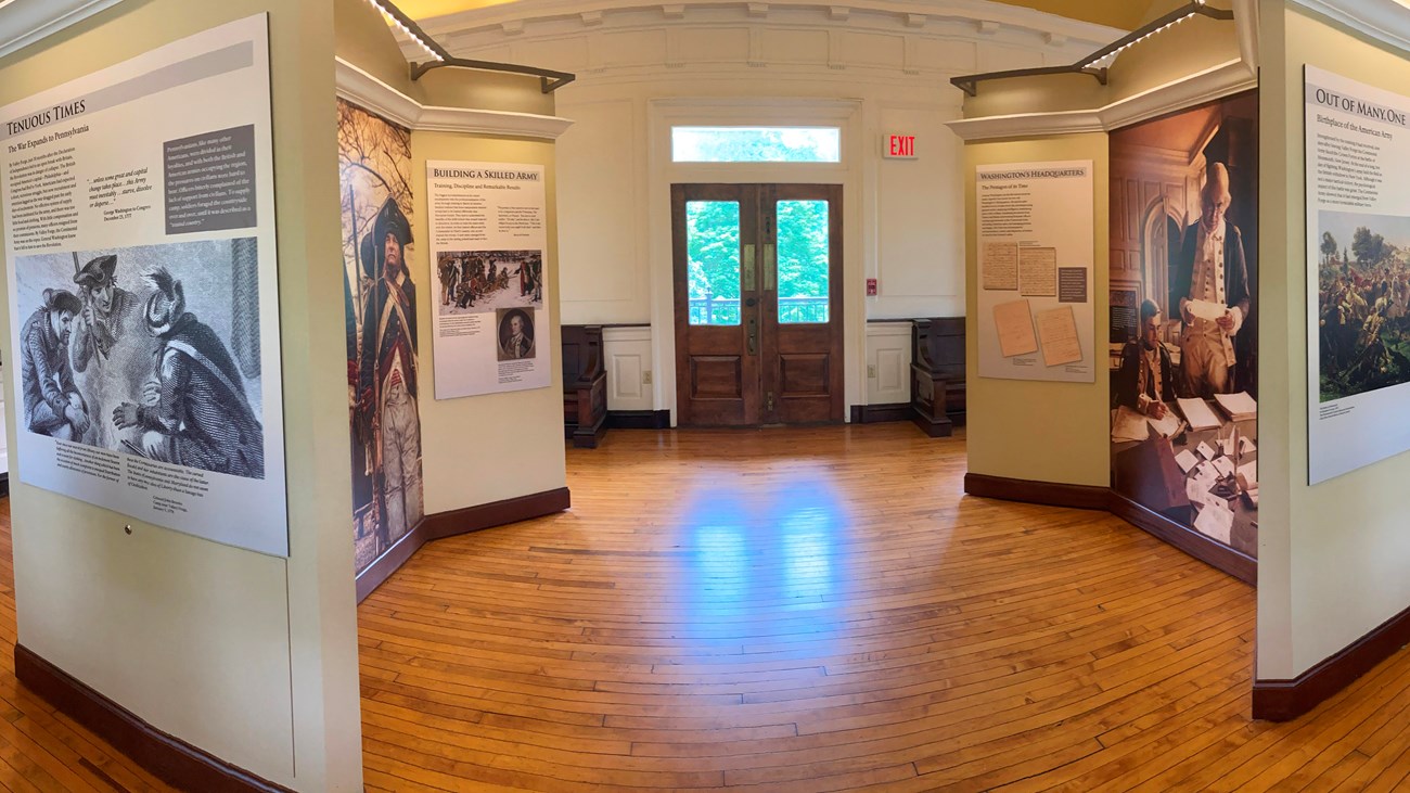 Exhibit panels with text and images are mounted on free-standing walls. wood-paneled floor