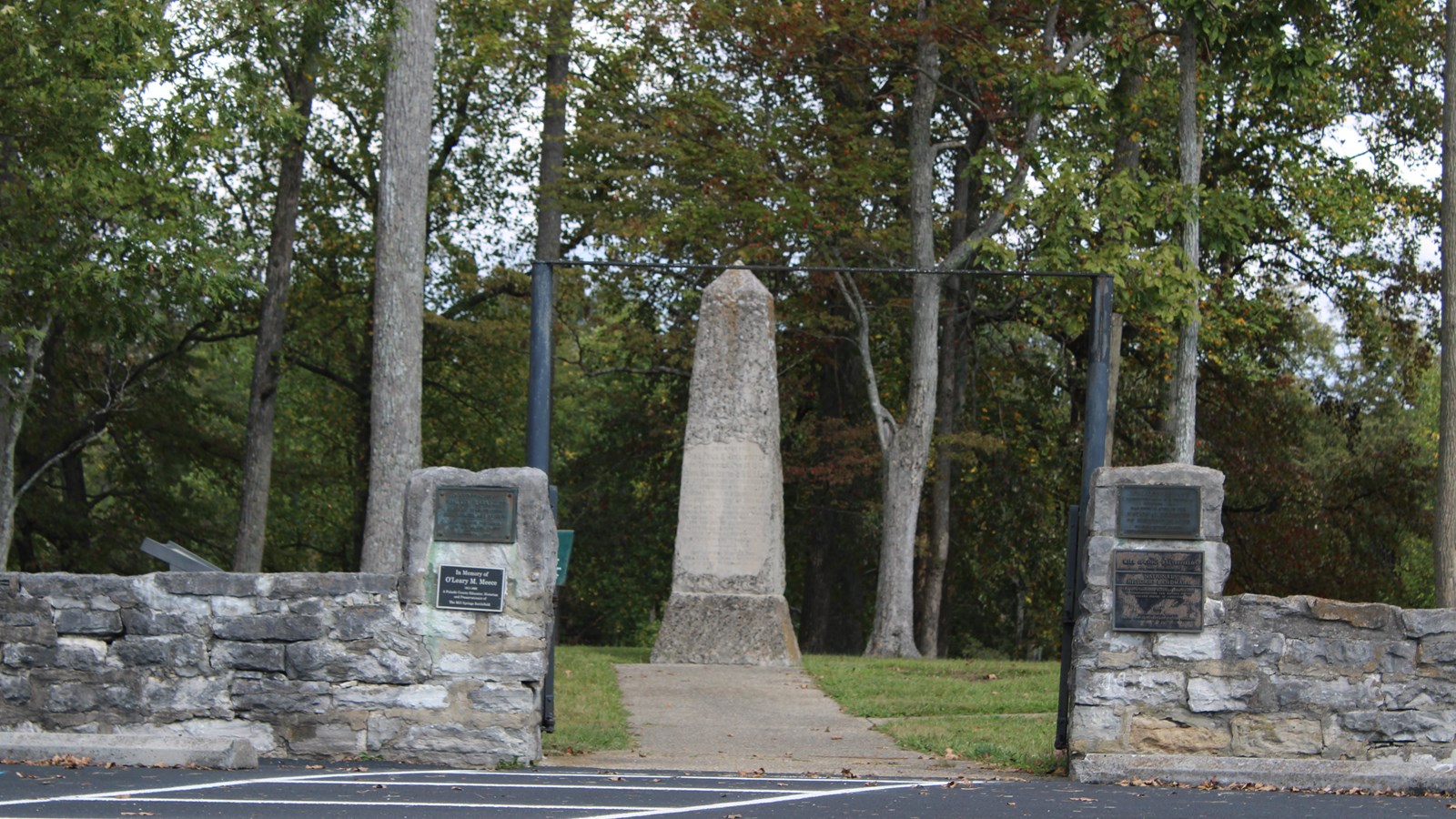 Parking lot in front of a historic wall and gate behind which is a small obelisk monument.