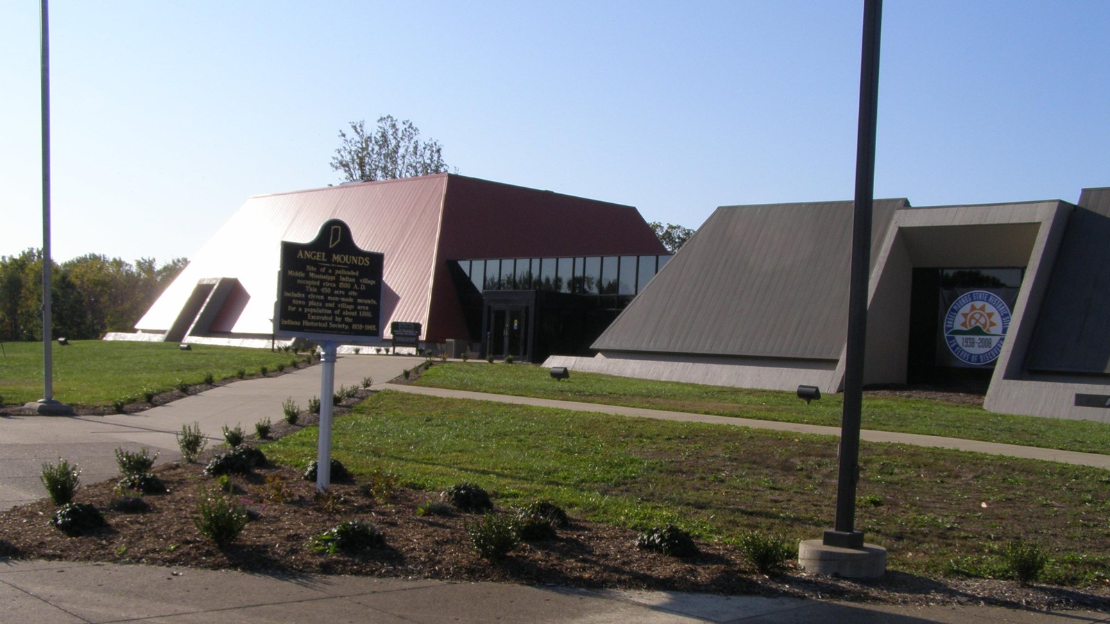 A large, angular building, a sign heading reads “Angel Mounds” in front of it.