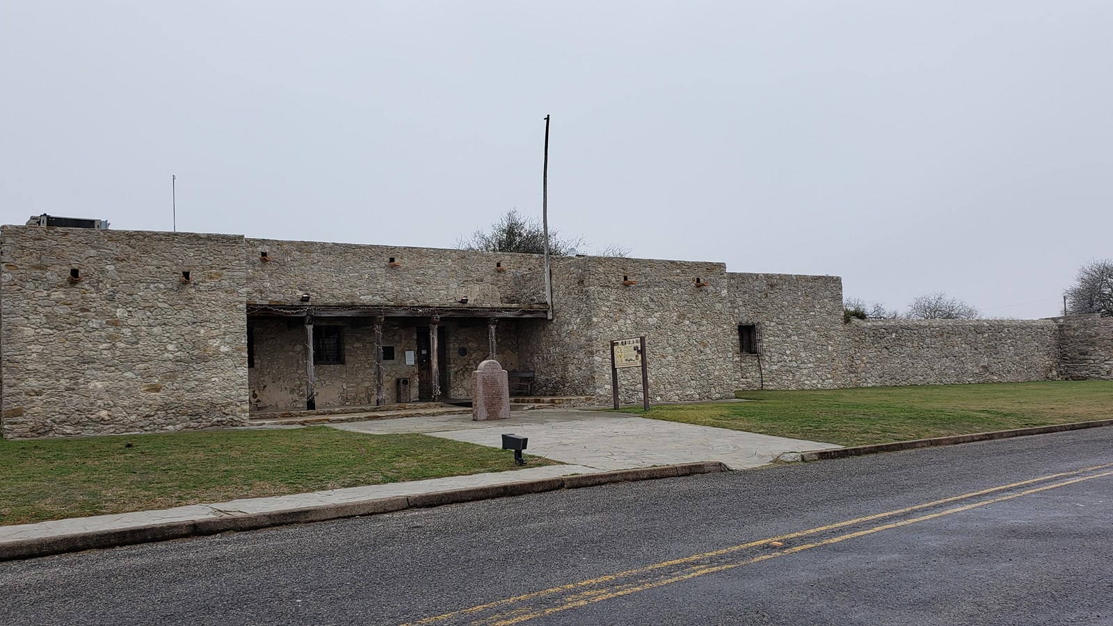 Historic stone structure with a small, covered entrance area and a wall, exhibit, and historical mar