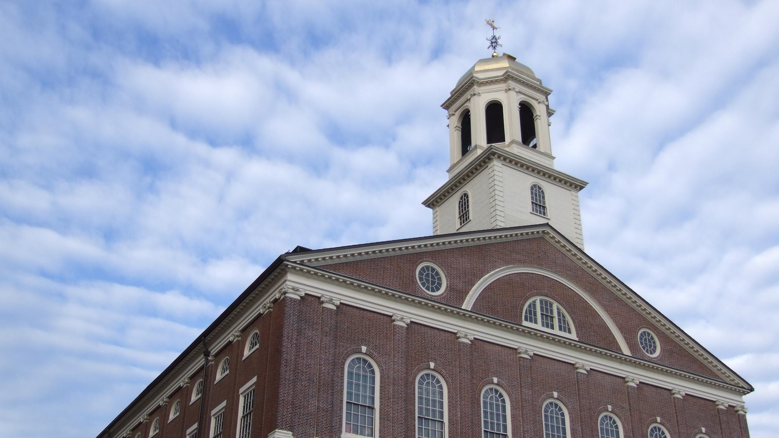 Photograph looking up at a brick building with a white cupola against a blue sky.