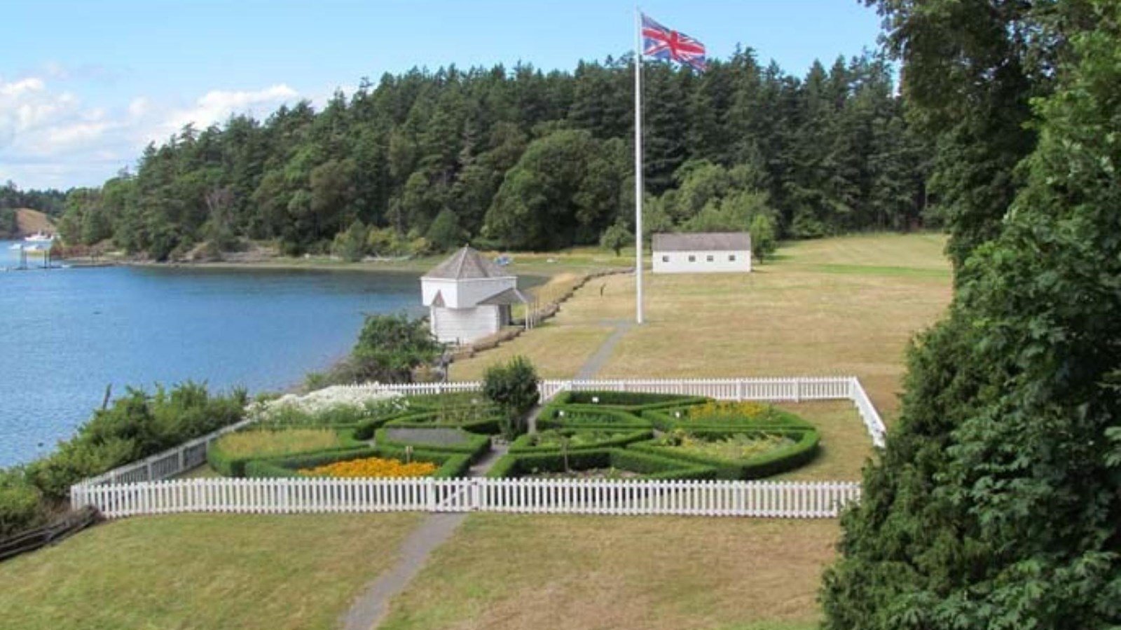 Color photo of a formal garden seen from above. Beyond the garden are wood frame structures.