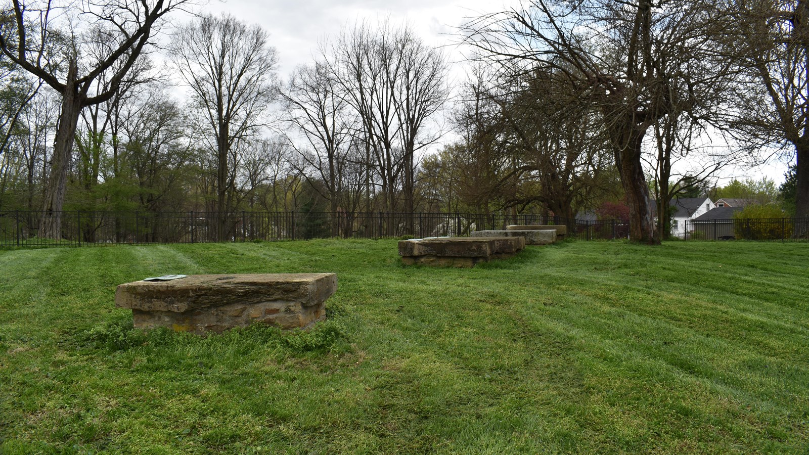 The photo shows a grassy field with a row of low, rectangular stone structures arranged in a line, e