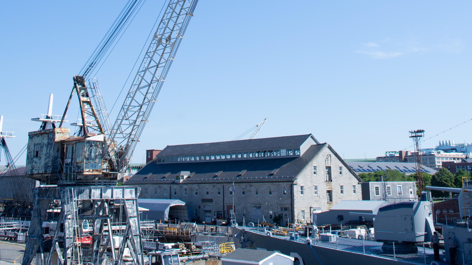 Photograph of a massive steel portal crane with a boom extending out of view. Stone warehouse behind