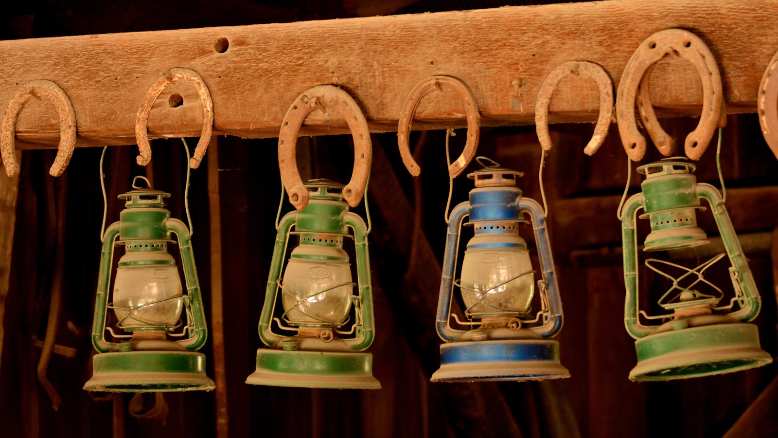 Four gas lanterns hang in a row from a wood cross beam in an 1800s style workshop.