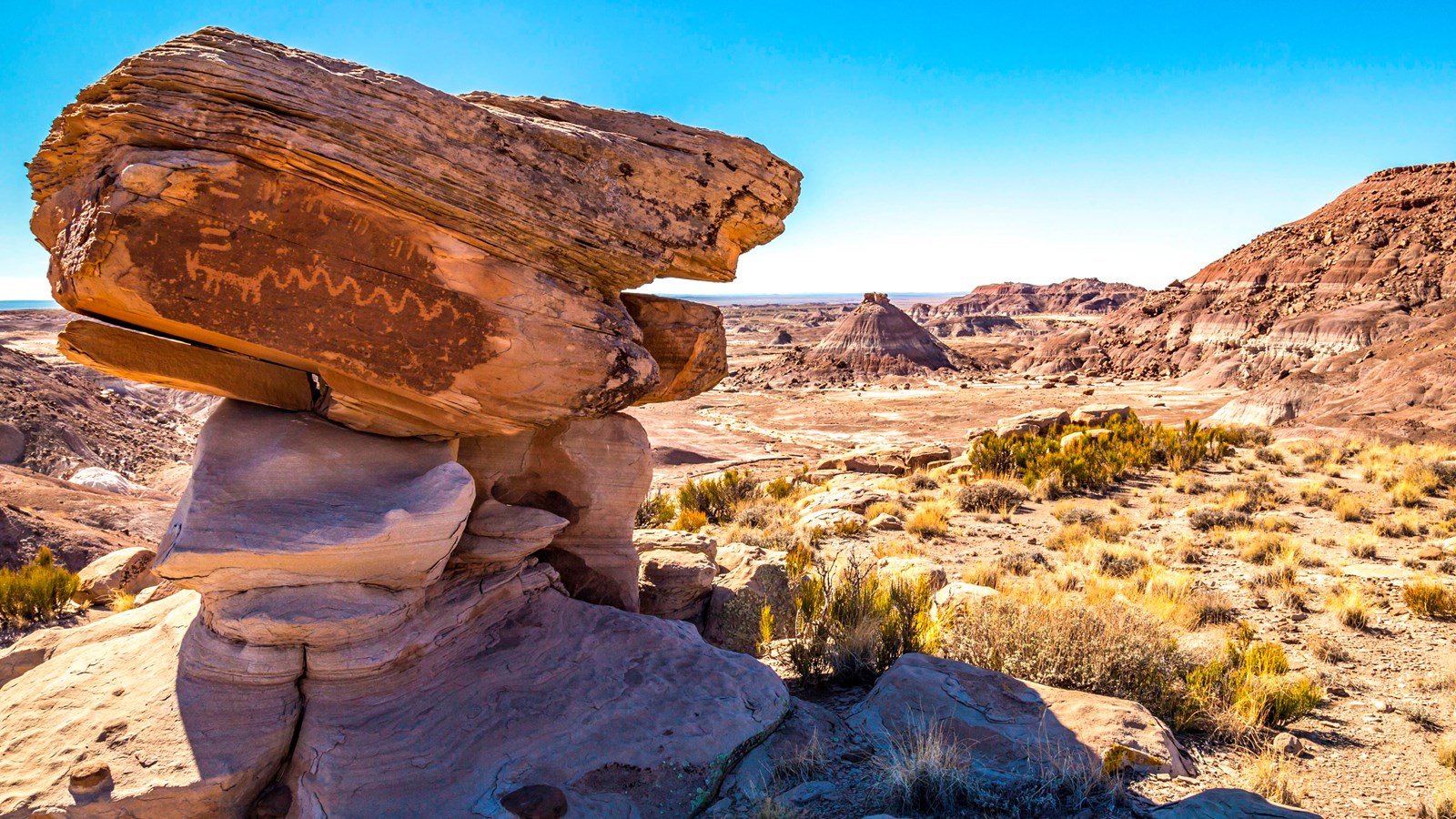 Rocks—some with petroglyphs—pile up throughout the scenic view with buttes and mesas under a blue sk