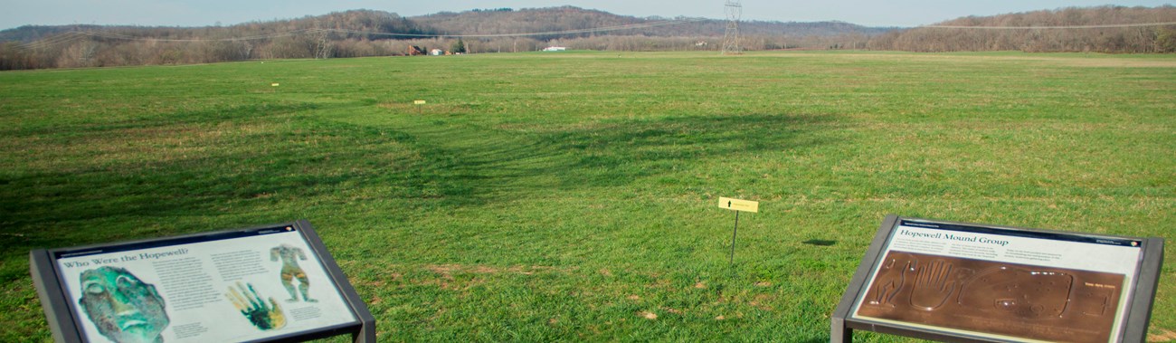 Two interpretive signs in the foreground with a large green field in the background