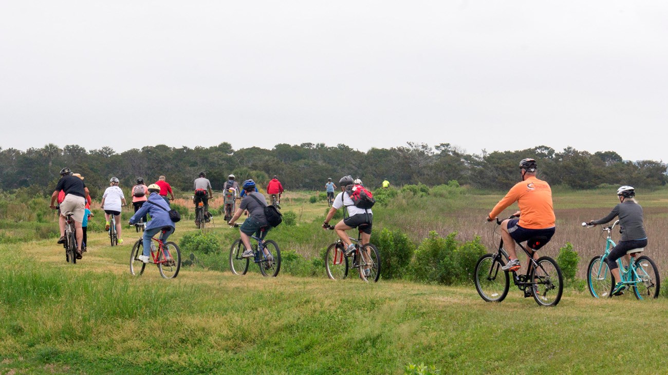 A large group of bike riders on an elevated grassy trail. 