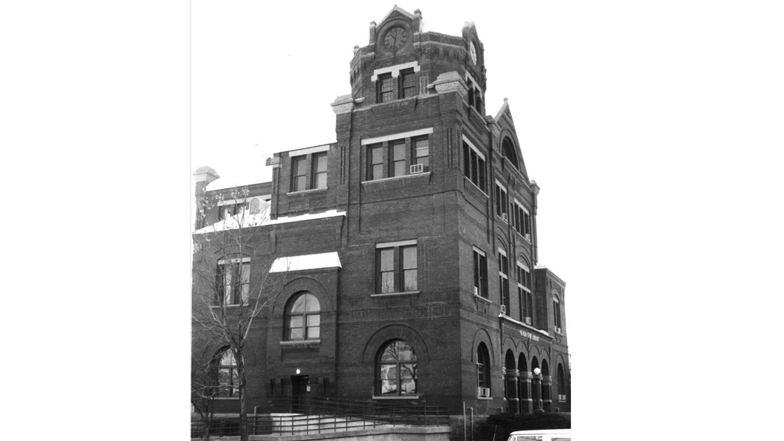 Historic black and white image of a tall, four story brick building with impressive roof facades.