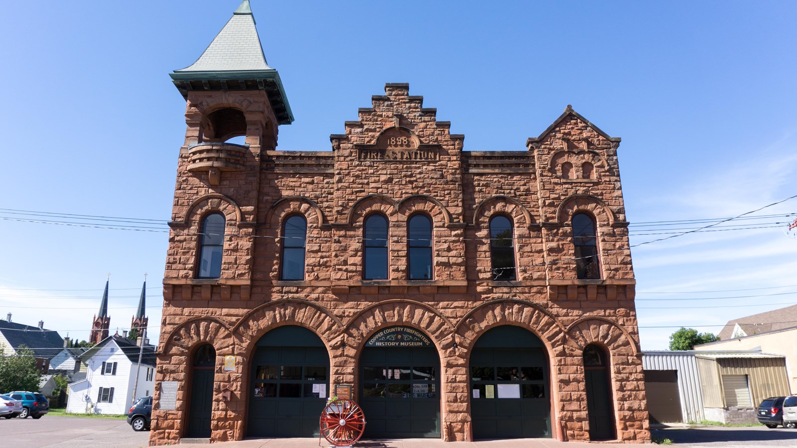 Summer scene of two-story sandstone building with tall triangular pergola and triangular false front