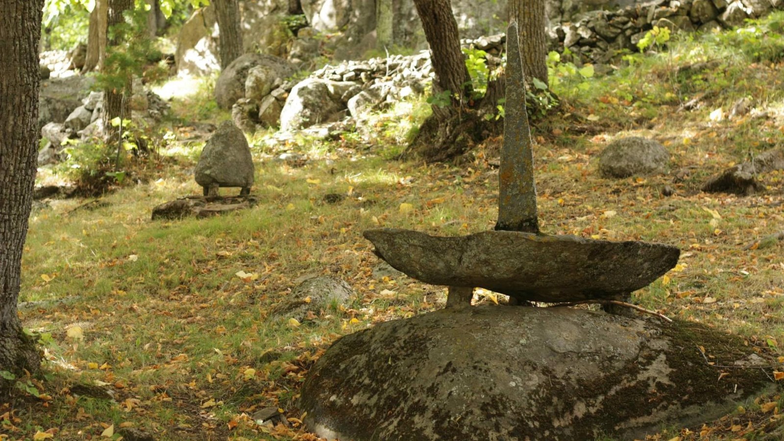 A rock sculpture is seen in the foreground of a wooded area. 3 rocks are stacked.