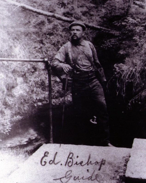 A black and white photo of a black man leaning against a handrail that descends behind him.