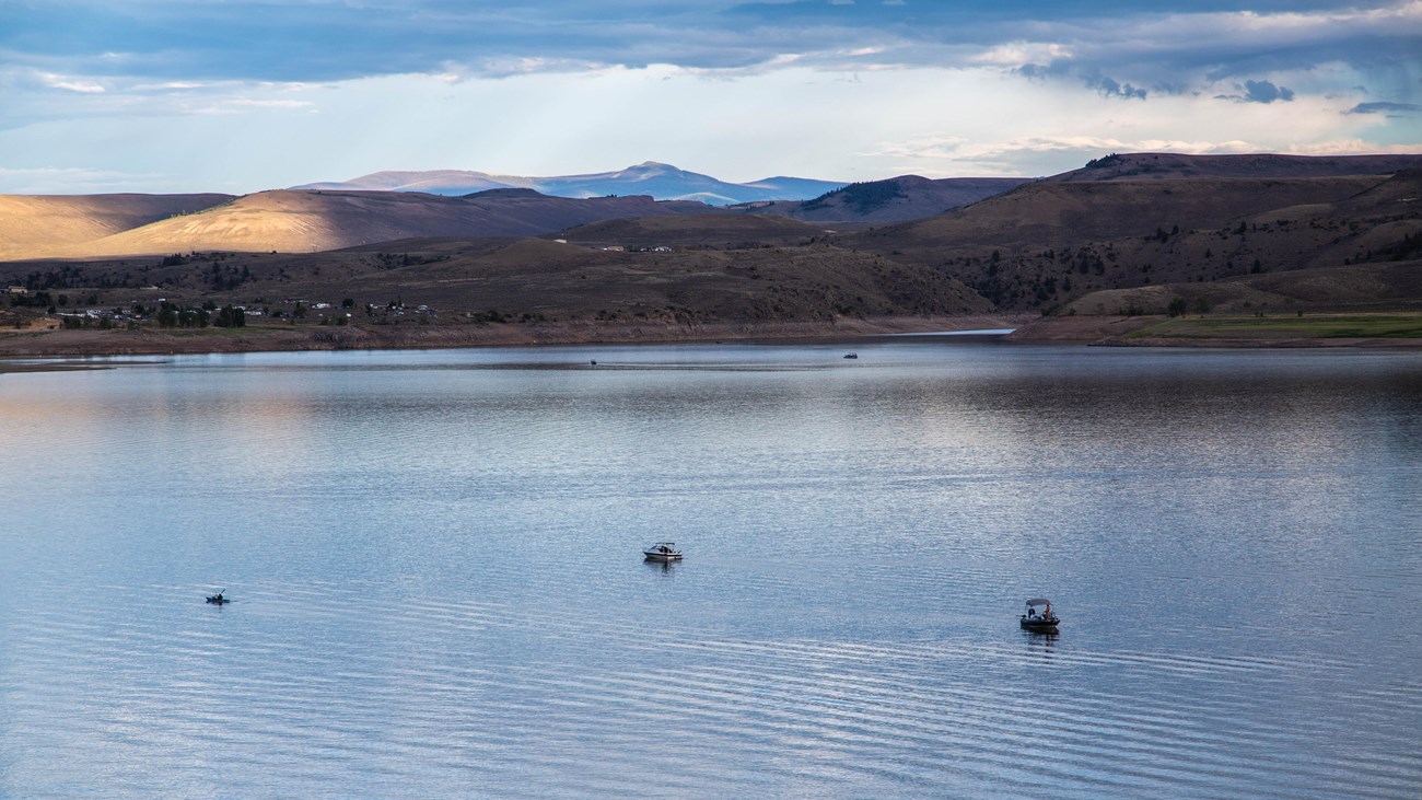Multiple boats on a still water reservoir with mountains in the background