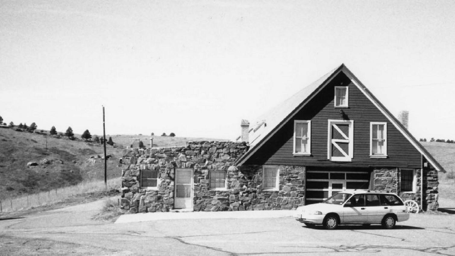 Two-story building with shiplap exterior and stone walls on a plain