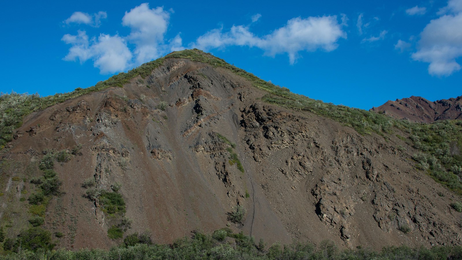 Dark orange and brown bands of rock cut through an exposed hillside of gray rock.