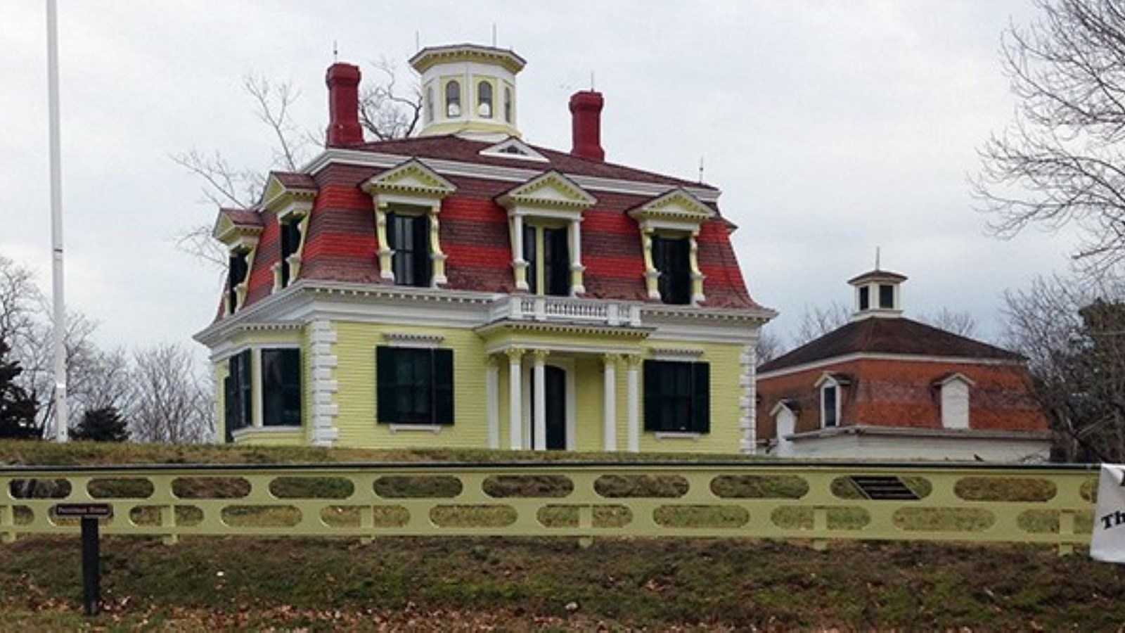 Yellow Victorian-style home with brown and red accents. Property surrounded by yellow fence.