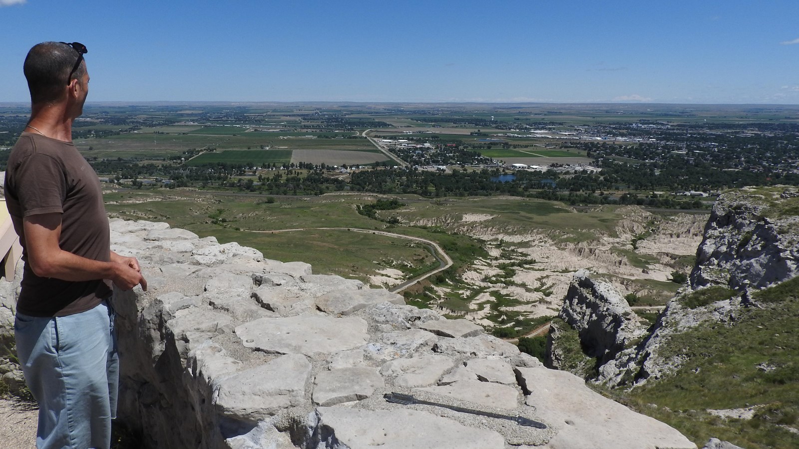 A man stands behind a low rock wall and admires the view of the North Platte River Valley.