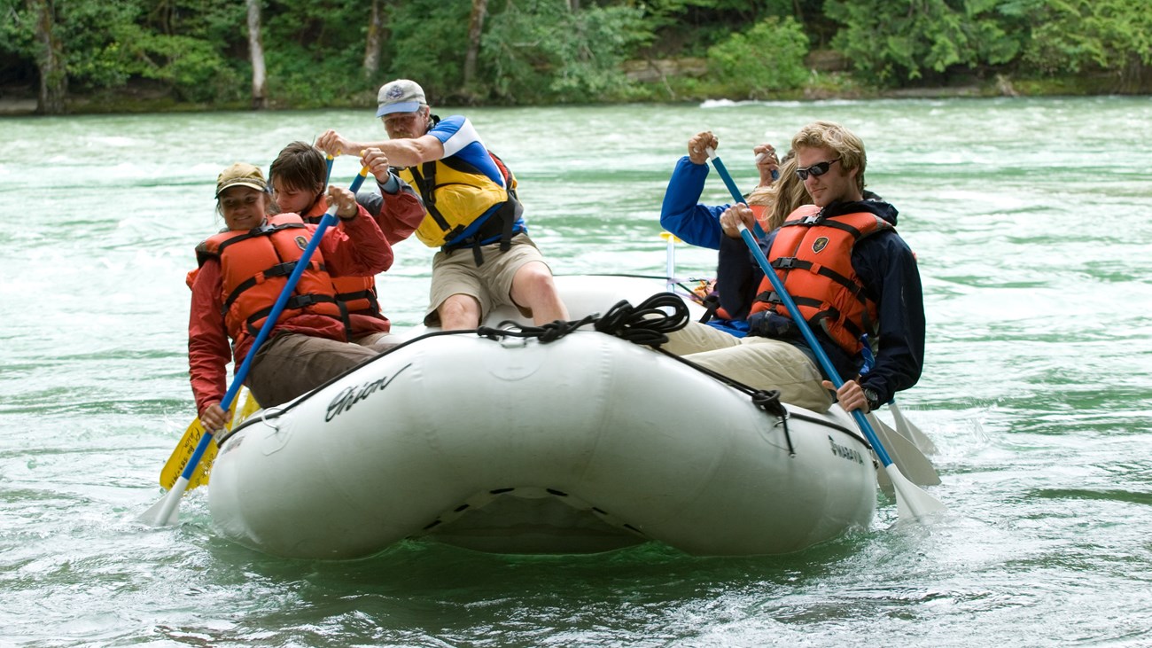 A group paddle a raft on a wide river.