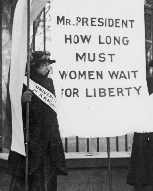 1917 photo of a woman holding a banner that says Mr President How Long Must Women Wait For Liberty