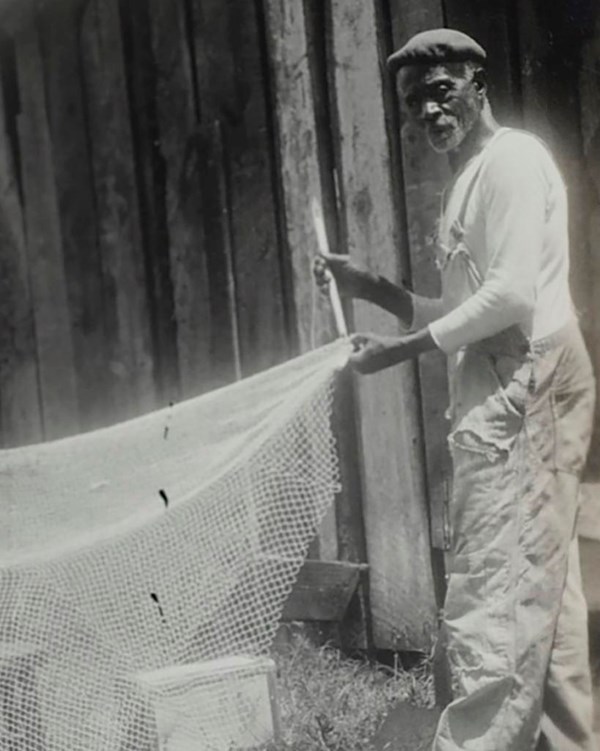 A historic photo of an elderly Black man working on a fish net