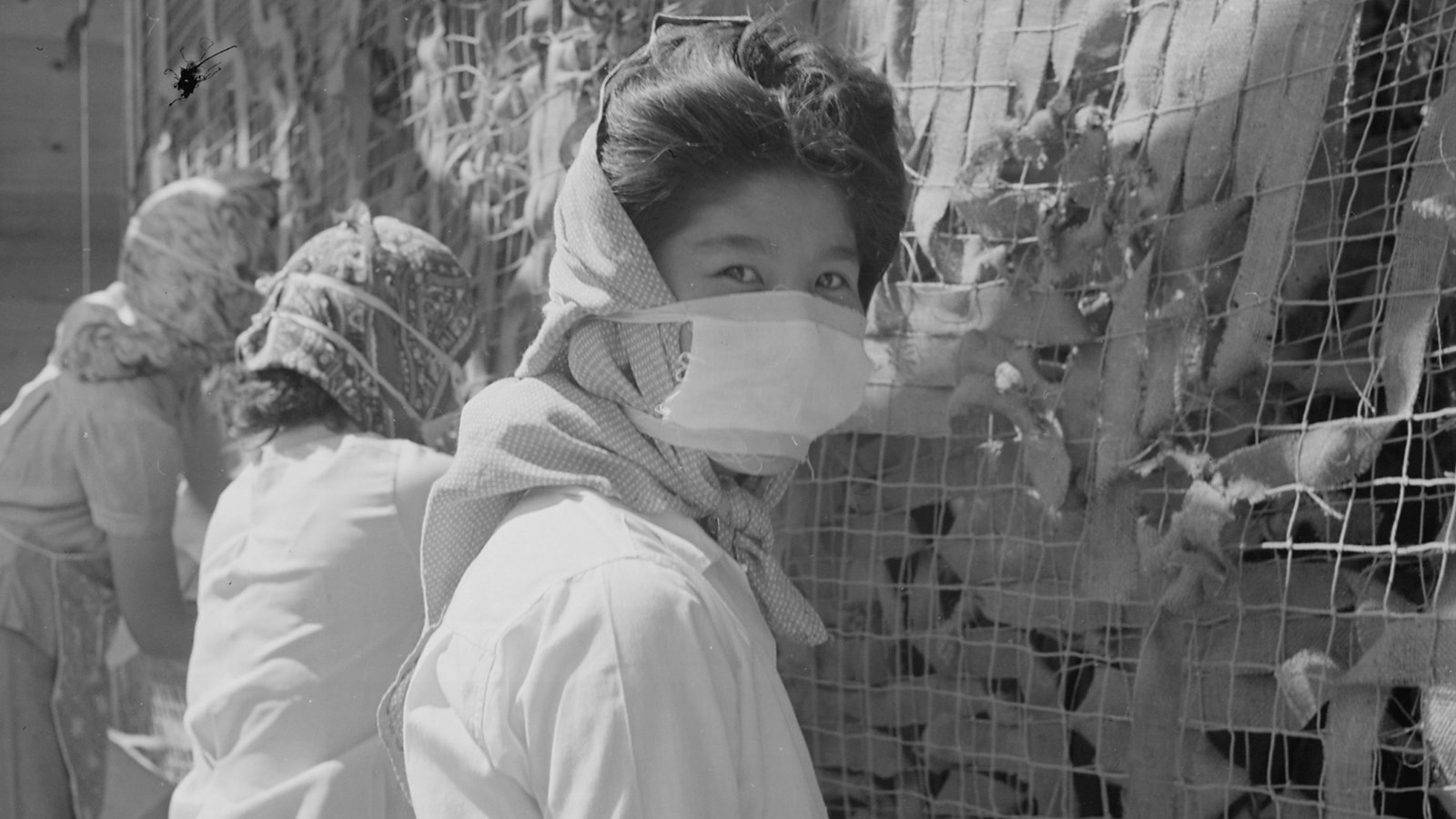 A black and white photo of a masked woman sitting in front of a net.