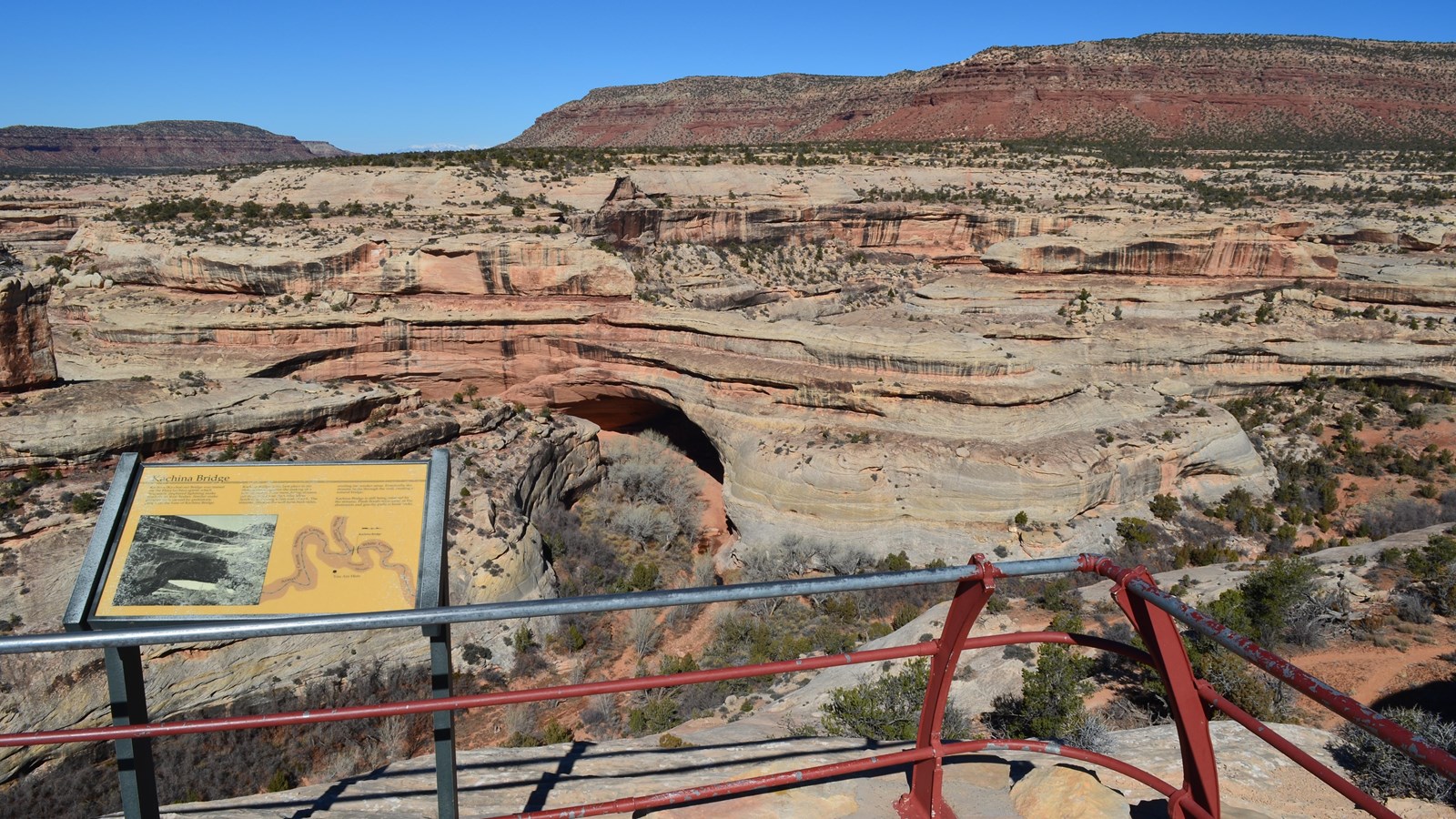 a paved platform with metal railing overlooking a natural sandstone bridge.