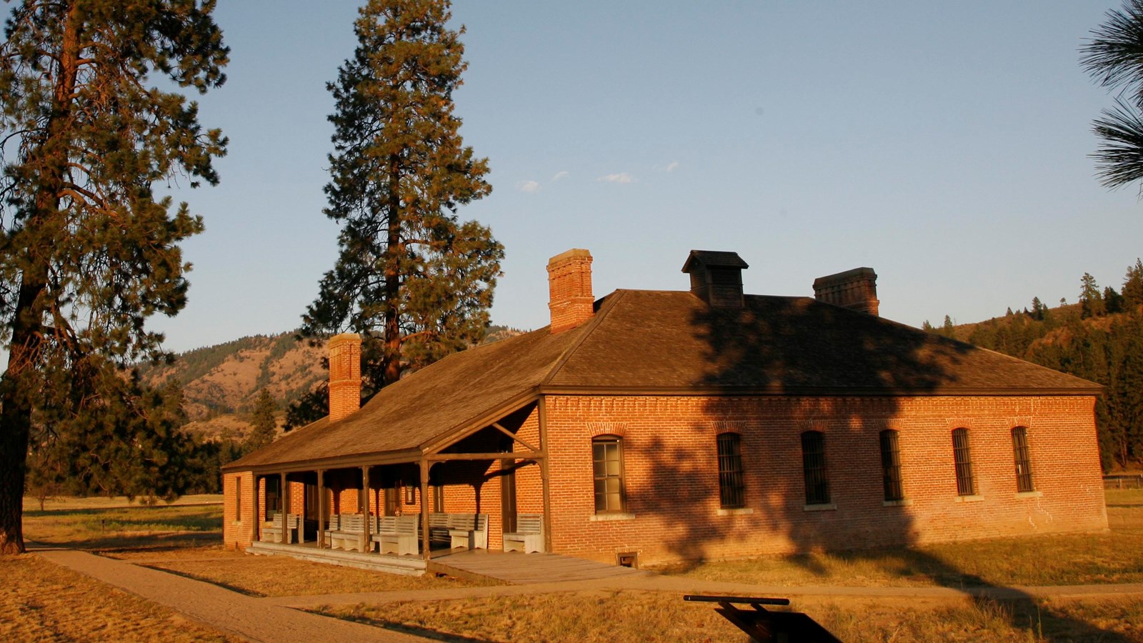 Sunset lit brick building surrounded by tall pine trees.