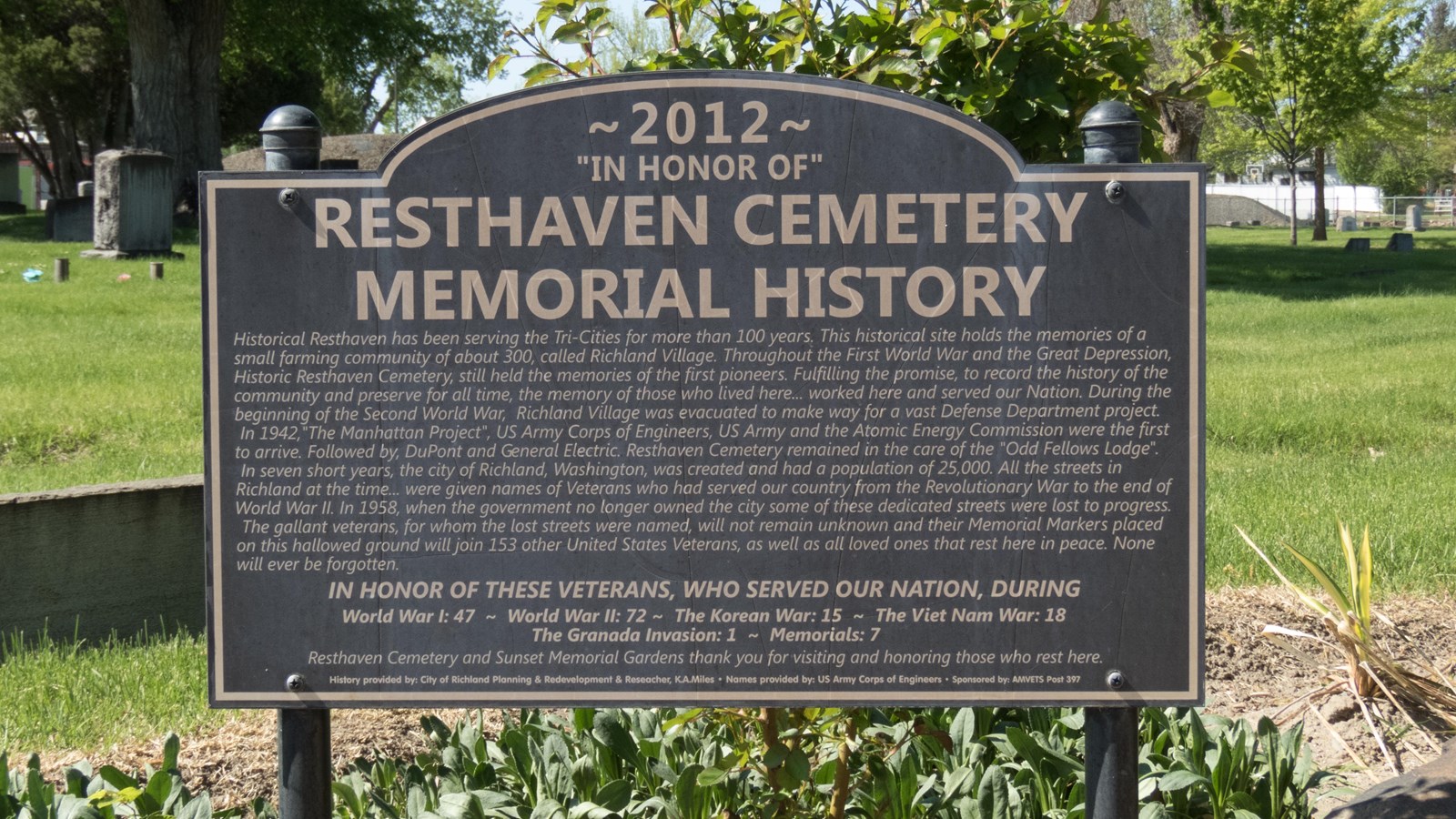 Color photograph of an informational sign next to a set of headstones. 