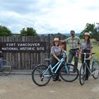 A group of people including park rangers stand by the Fort Vancouver entrance sign with their bikes.