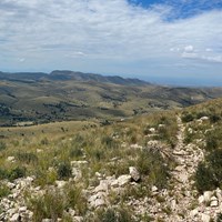 From a high point, a desert grasslands stretches into the distance with ridges in the background.