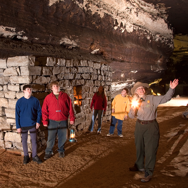 Visitors on the lantern tour in Mammoth Cave explore a stone hut ruin by lantern light.