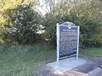 A upright sign sits in front of a wooded area.