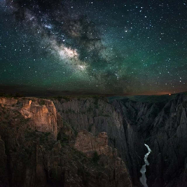 A dark, star-filled sky and Milky Way arch over Black Canyon of t he Gunnison National Park